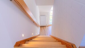 A staircase with wooden steps and white walls, leading to a room with a window and a radiator. - Vacation apartment Stöfs - Baltic Sea vacation. Close to the beach. Nature. Lake view. (Behrensdorf)