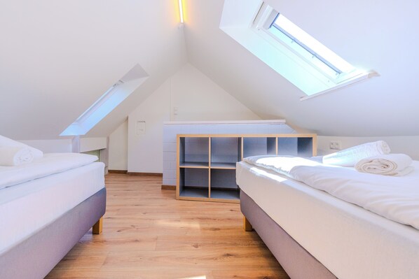 A modern, well-lit room with a sloped ceiling, two beds, a built-in wardrobe, and skylights. - Vacation apartment Stöfs - Baltic Sea vacation. Close to the beach. Nature. Lake view. (Behrensdorf)