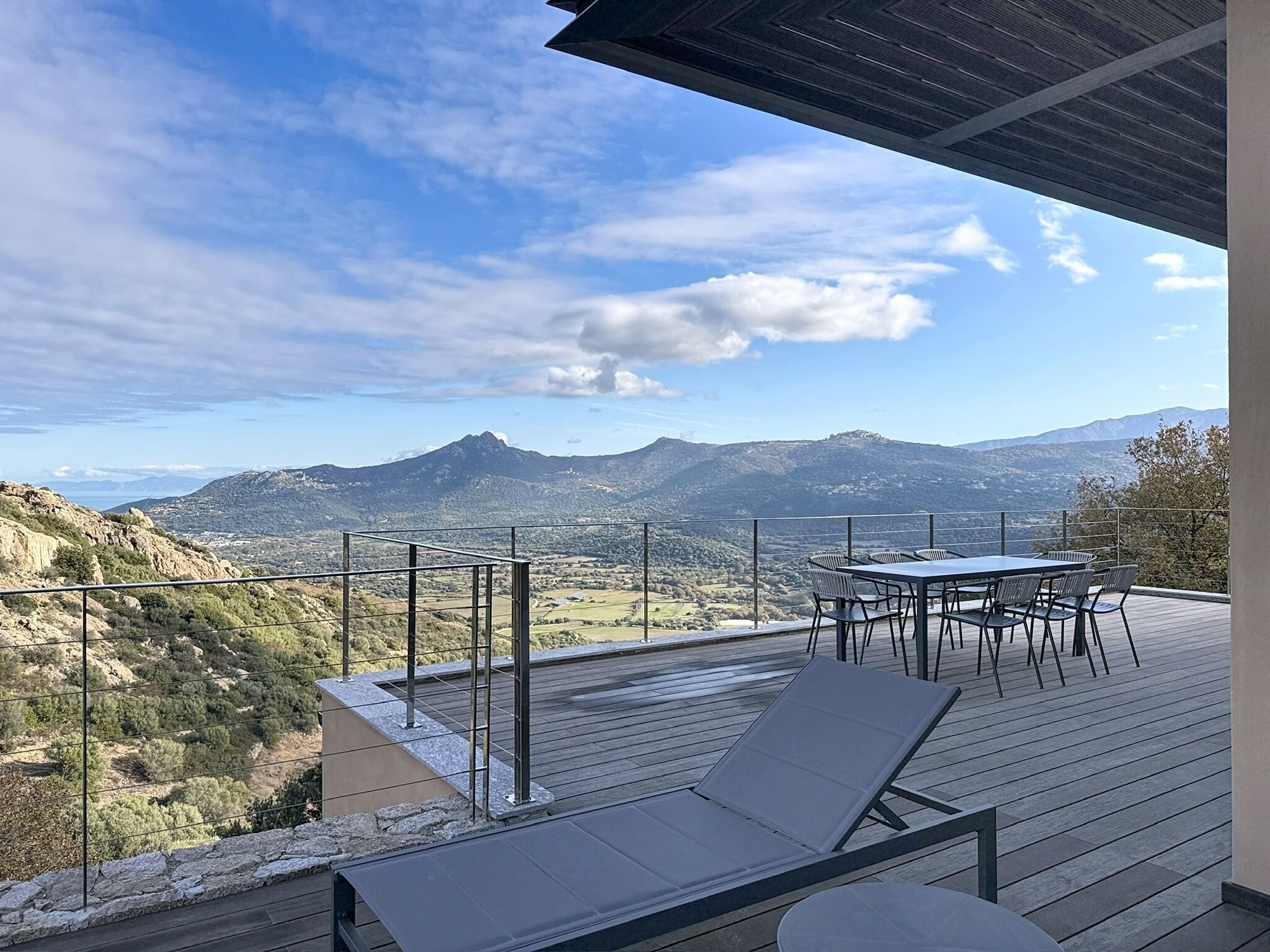 A deck with a table and chairs, overlooking a mountainous landscape.