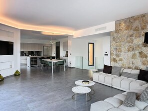 A modern living room with a sofa, two round tables, and a dining area with chairs. - Luxury villa, infinity pool, panoramic mountain view (Lumio)