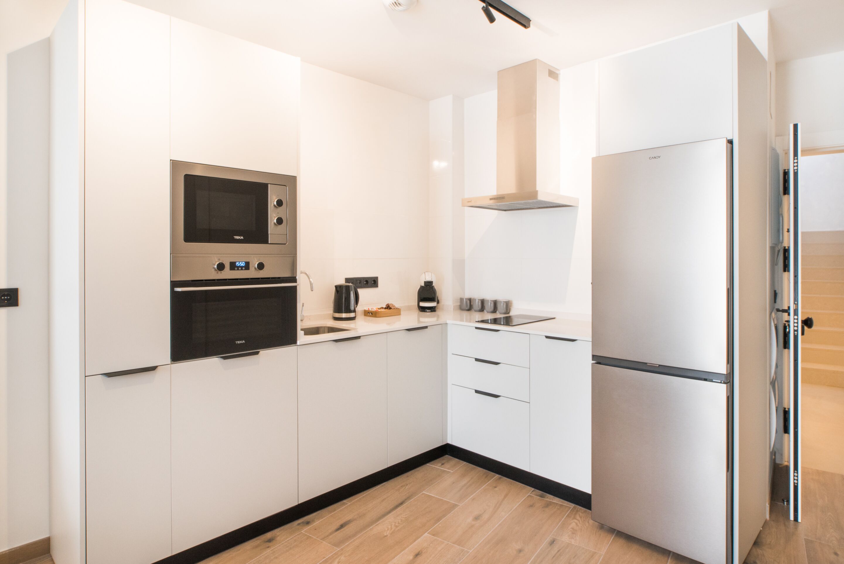 Una cocina moderna con armarios blancos, horno de acero inoxidable, microondas, estufa integrada y refrigerador.