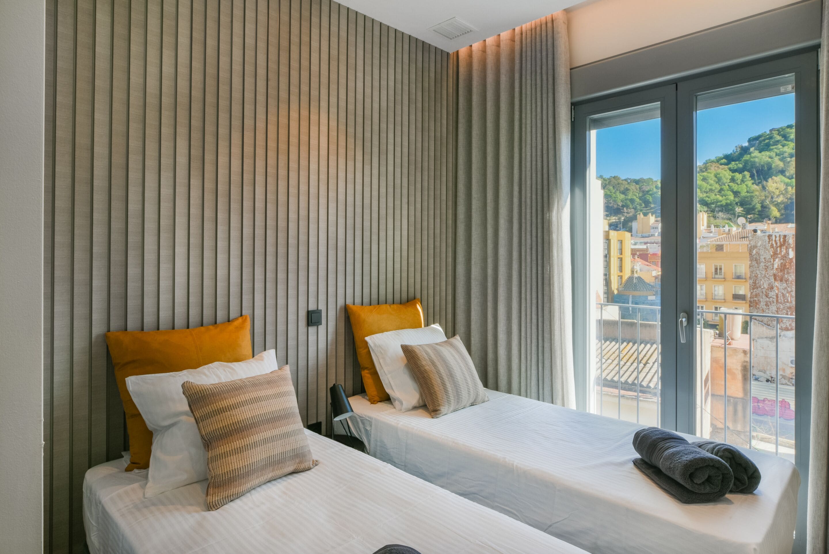 A hotel room with two beds, a large window with a city view, and a striped wall.