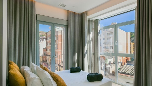Une chambre d’hôtel avec un grand lit, des rideaux et une vue sur les immeubles par la fenêtre.