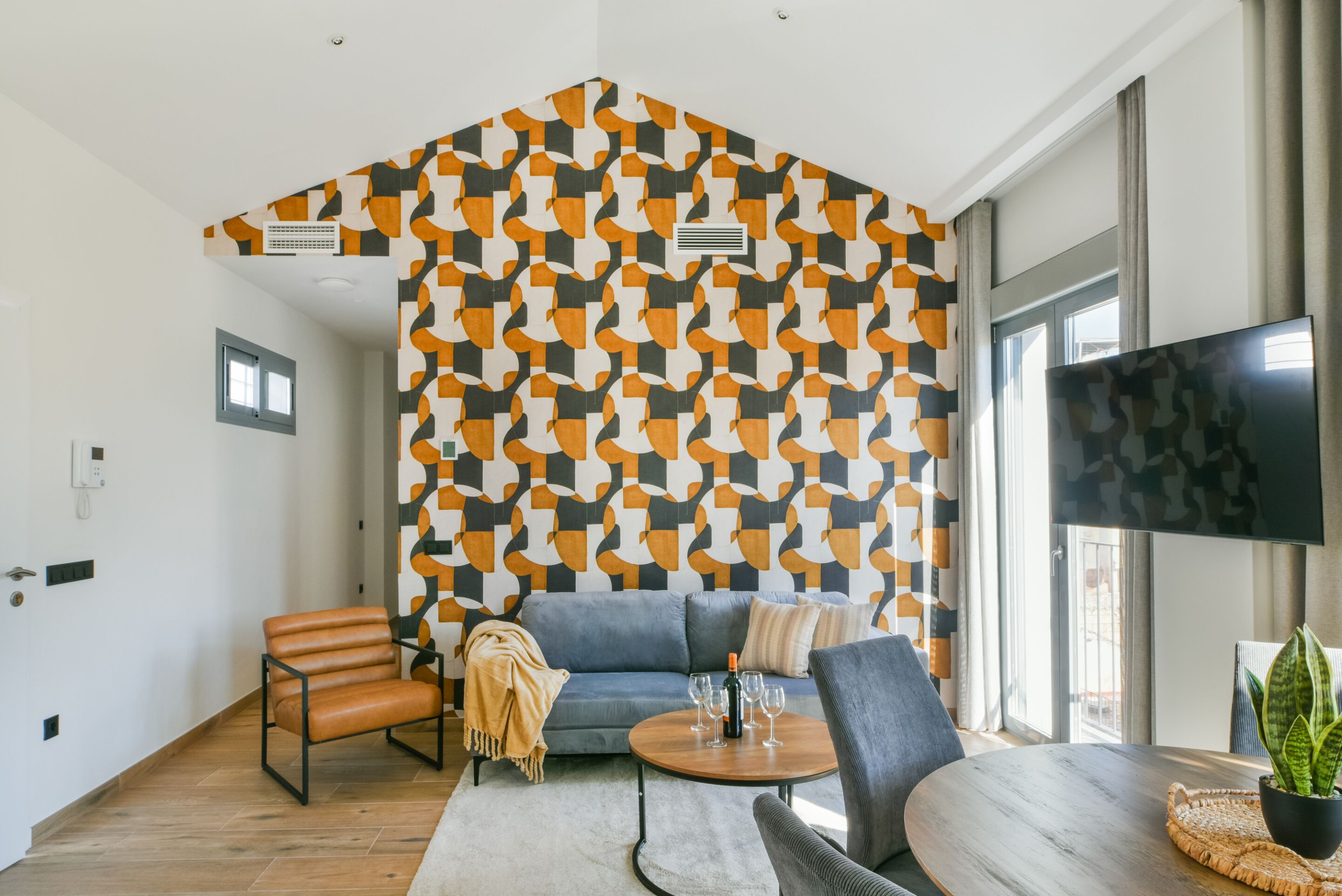 A modern living room with a geometric patterned wall, a sofa, a coffee table, and a television.