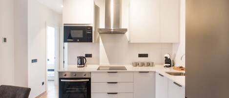 Una cocina moderna con gabinetes blancos, una campana extractora de acero inoxidable, horno empotrado, microondas y refrigerador.