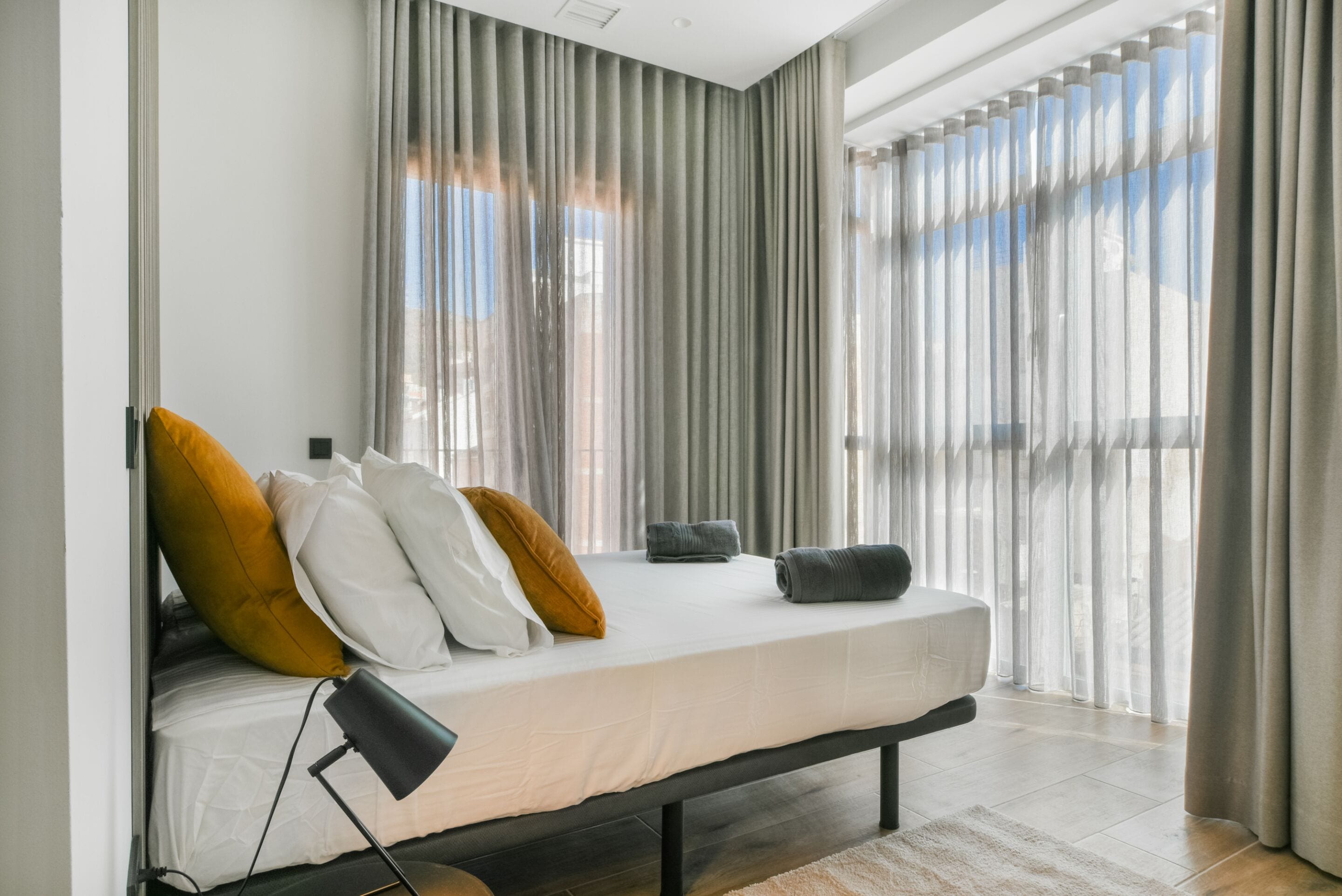 A modern bedroom with a bed, curtains, and a view through the window.