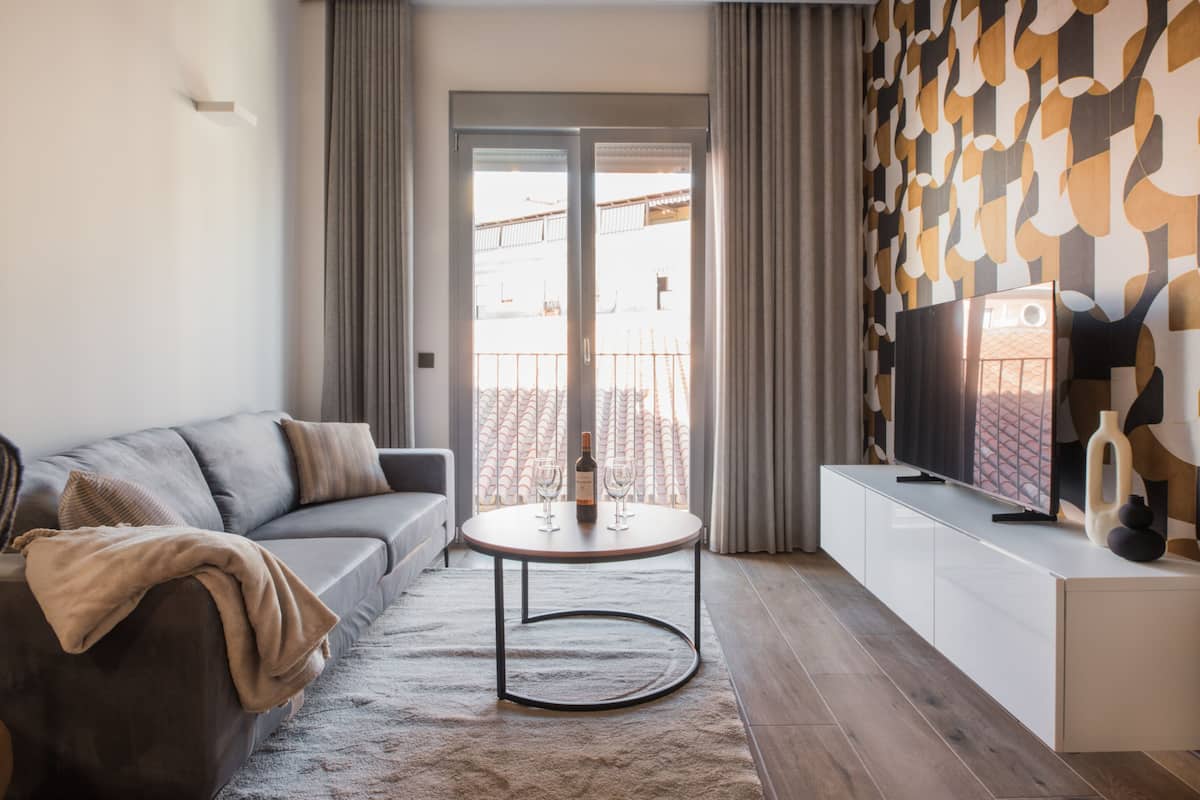 En moderne stue med en sofa, et rundt bord, et fladskærms-tv og en tapetseret væg.