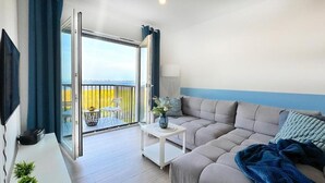 A modern living room with a sofa, a small table with a vase, a TV, and a balcony with a view. - Lake view apartment Dziwnow (Dziwnów)