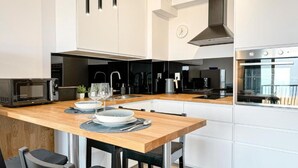 A modern kitchen with white cabinetry, a wooden countertop, a microwave, a kettle, and a view of the city through the window. - Lake view apartment Dziwnow (Dziwnów)