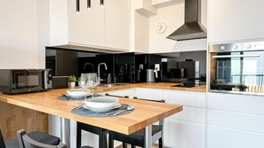 A modern kitchen with white cabinetry, a wooden countertop, a microwave, a kettle, and a view of the city through the window. - Lake view apartment Dziwnow (Dziwnów)