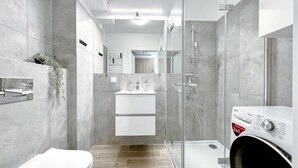 A modern bathroom with a glass shower enclosure, a built-in sink, and a washing machine. - Lake view apartment Dziwnow (Dziwnów)