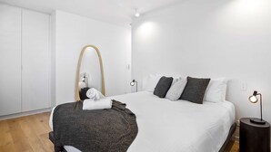 Una habitación de hotel moderna con una cama grande, un espejo redondo, lámparas de noche y un armario.