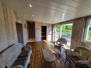 A wooden deck with wicker furniture, a shower area, and a glass door leading to an outdoor seating area.
