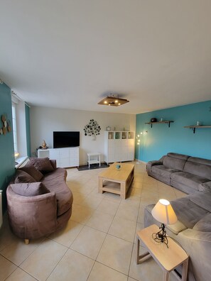 A living room with a sofa, a coffee table, a TV, a cabinet, and a lamp. - 8-person gîte with sauna and garden (Anor)
