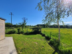 A rural landscape with a field, a wooden structure, and a tree.