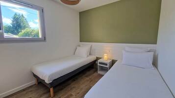 Een kleine kamer met een enkel bed, een raam, een nachtkastje met lamp en een groene accentmuur.