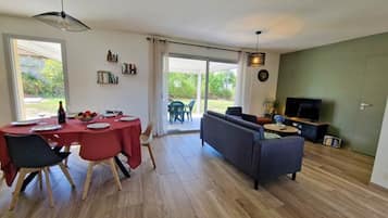 Een moderne woonkamer met een bank, televisie en een eethoek met een tafel gedekt voor twee personen.