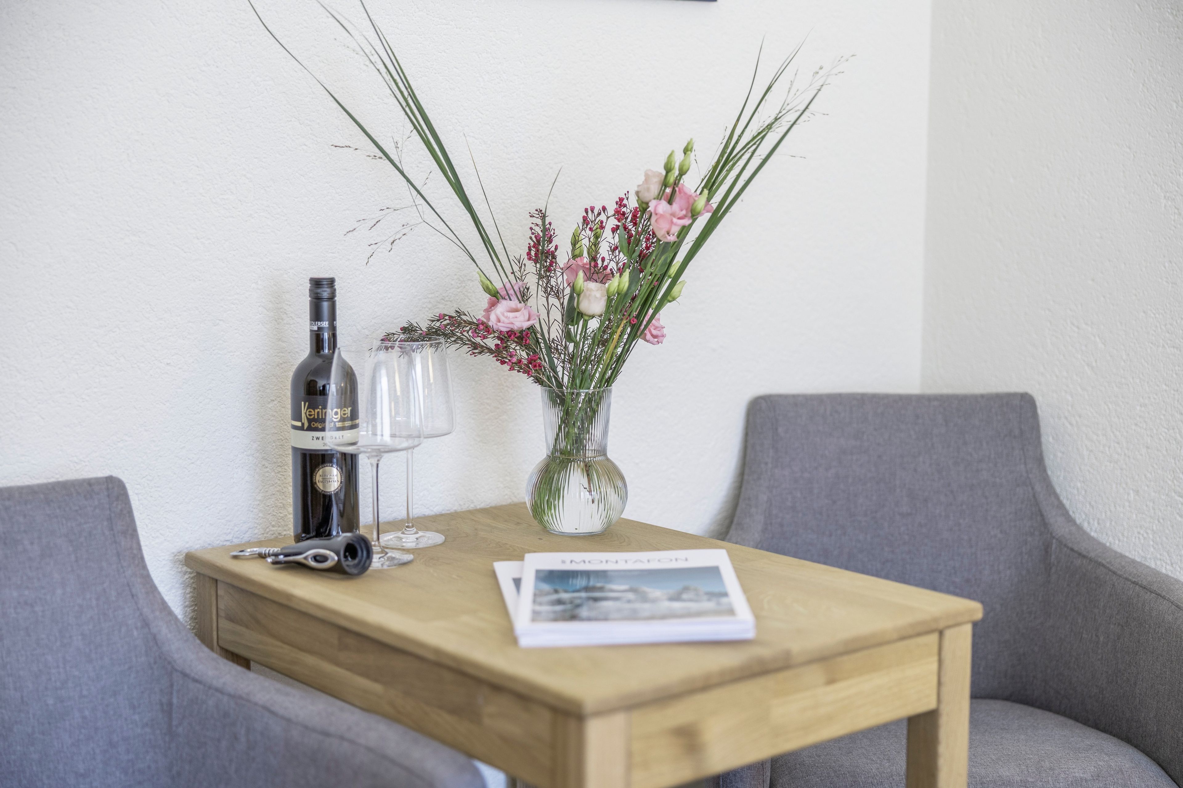A wooden table with a bottle of wine, a glass, and a vase with flowers.