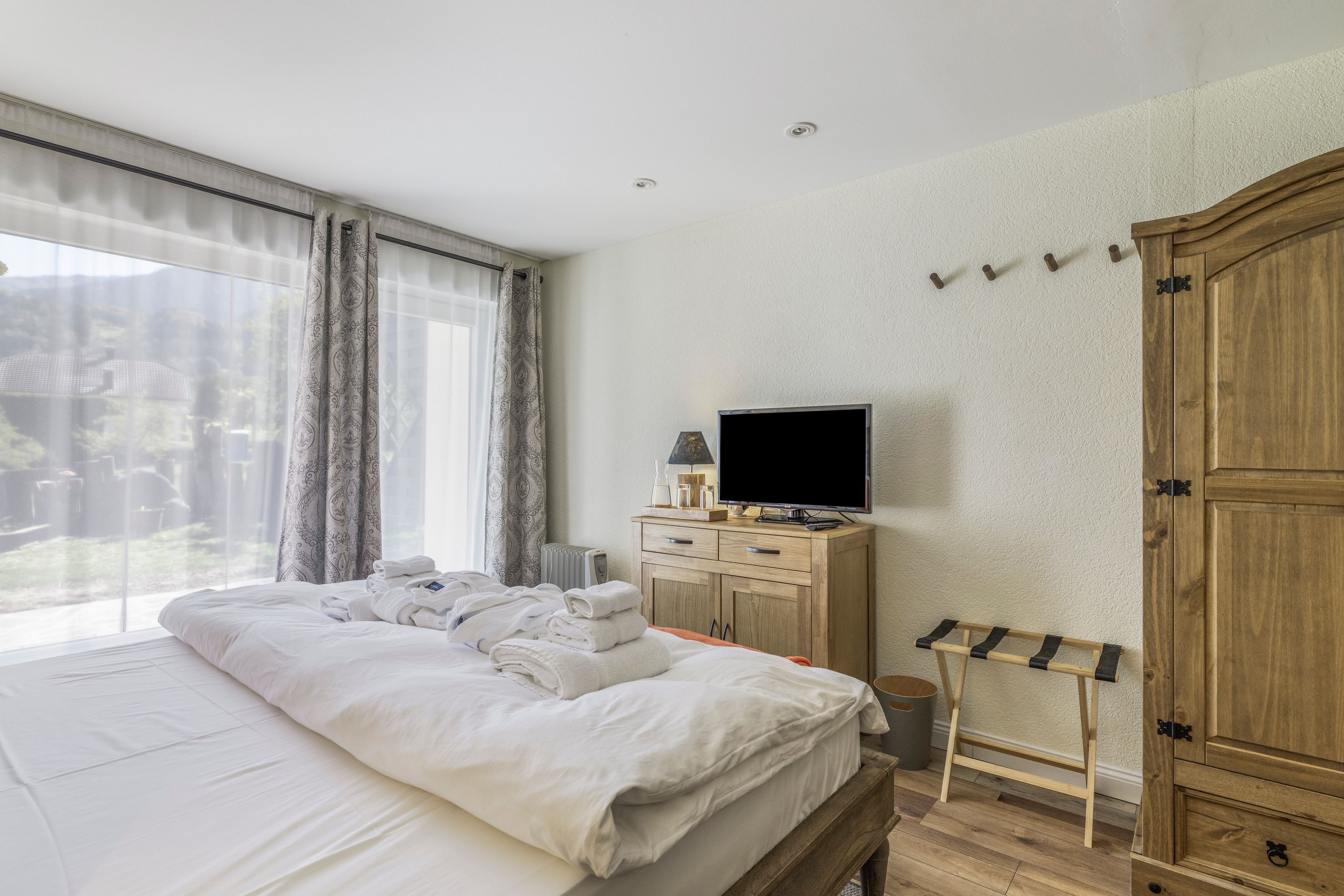 Ett hotellrum med en säng, en tv, en garderob i trä och ett fönster med gardiner.