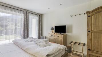 Ett hotellrum med en säng, en tv, en garderob i trä och ett fönster med gardiner.