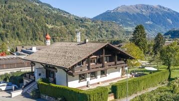 A chalet-style building with a sloped roof, wooden balconies, and a view of a mountainous landscape.