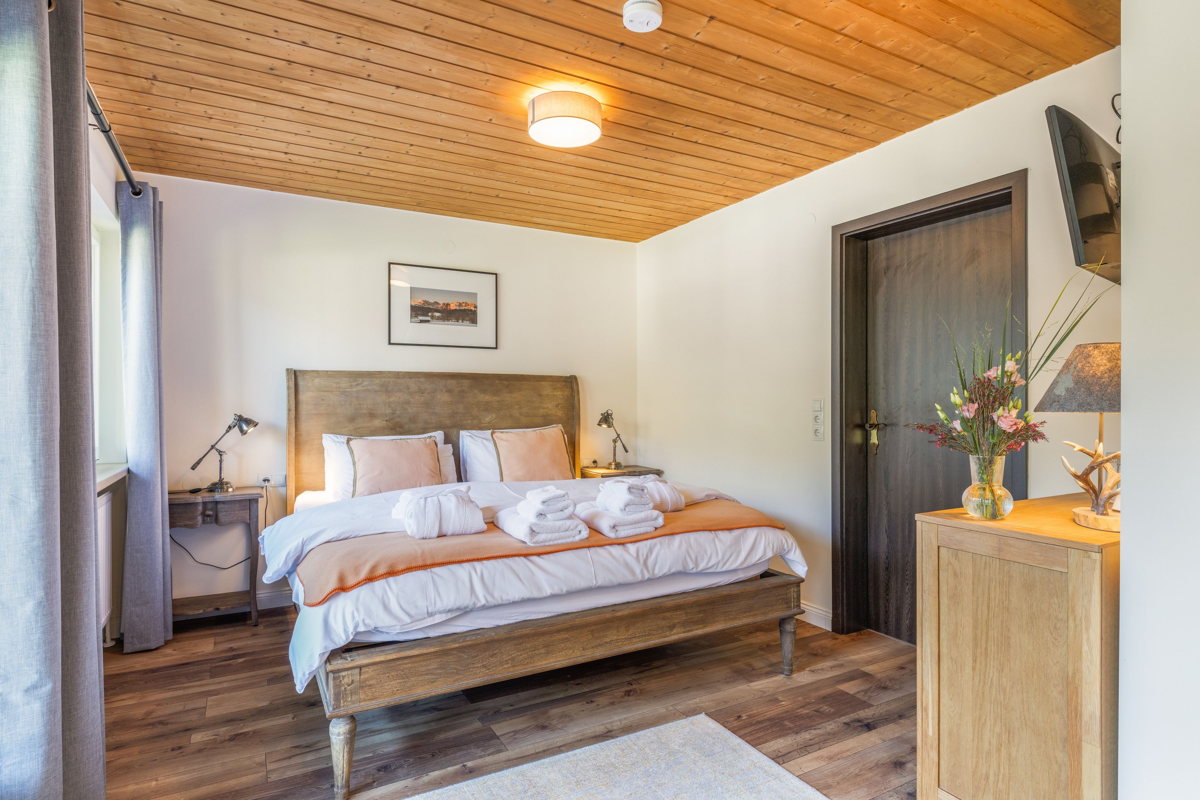 Une chambre à coucher avec une tête de lit en bois, un lit recouvert de draps blancs, une table de chevet avec une lampe et une porte en bois.