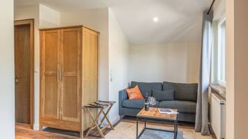 A room with a wooden wardrobe, a grey sofa, a small wooden table with a magazine, and a radiator.