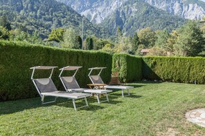 A garden with three lounge chairs and a table, surrounded by neatly trimmed hedges and a mountain backdrop. - Chalet Suite with Breakfast, Mountain Views & Private Terrace (Vandans)