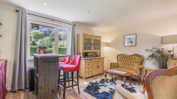 A cozy living room with a wooden dining table, red bar stools, a cream sofa, and a peacock feather decoration.