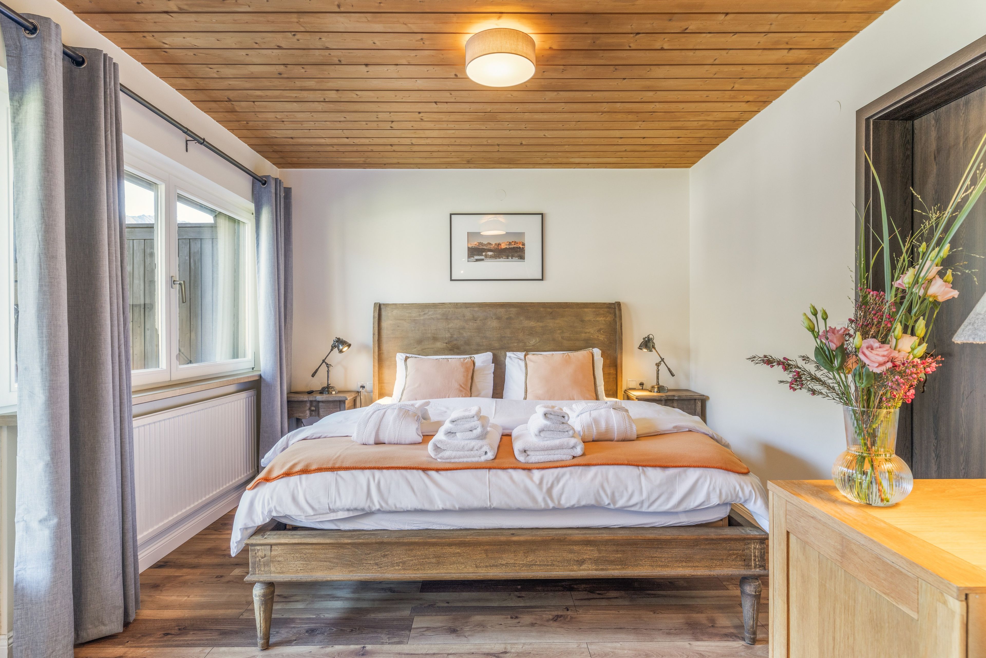 A neatly made bed with white linens, a wooden headboard, and a framed picture above it.
