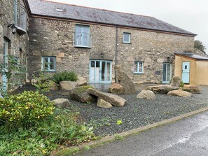 A stone building with a gravel driveway, large rocks, and greenery. - Rest, Reconnect & Gather at a Historic Cornish Barn (Saint Clether)