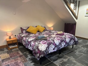 Une chambre à coucher avec une couvre-lit à motifs floraux, deux lampes de chevet, une table de chevet avec une lampe, un tapis à motifs et un escalier.