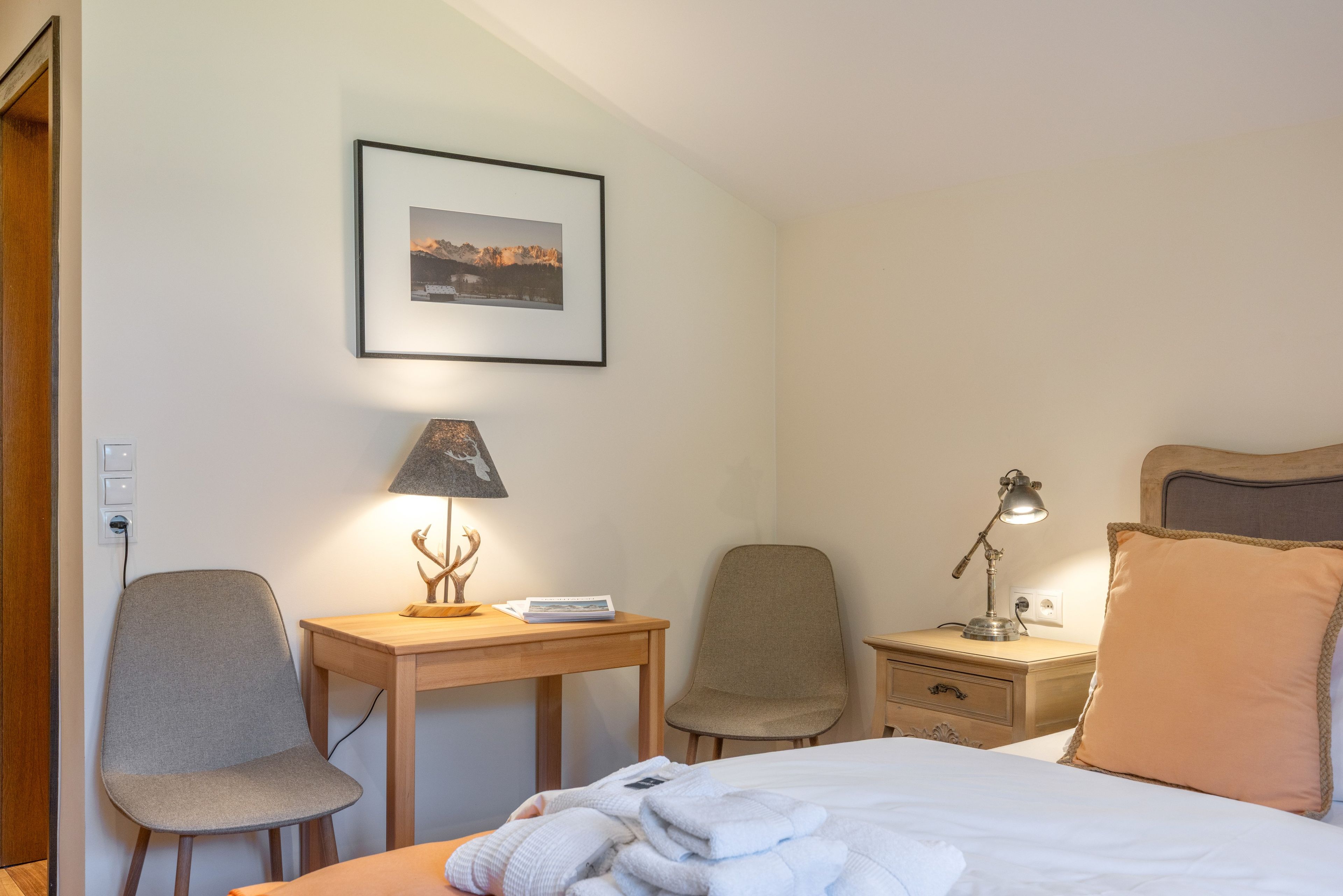 Ein Hotelzimmer mit einem Bett, zwei Stühlen, einem Schreibtisch, einem Nachttisch, einer Lampe und einem gerahmten Bild an der Wand.