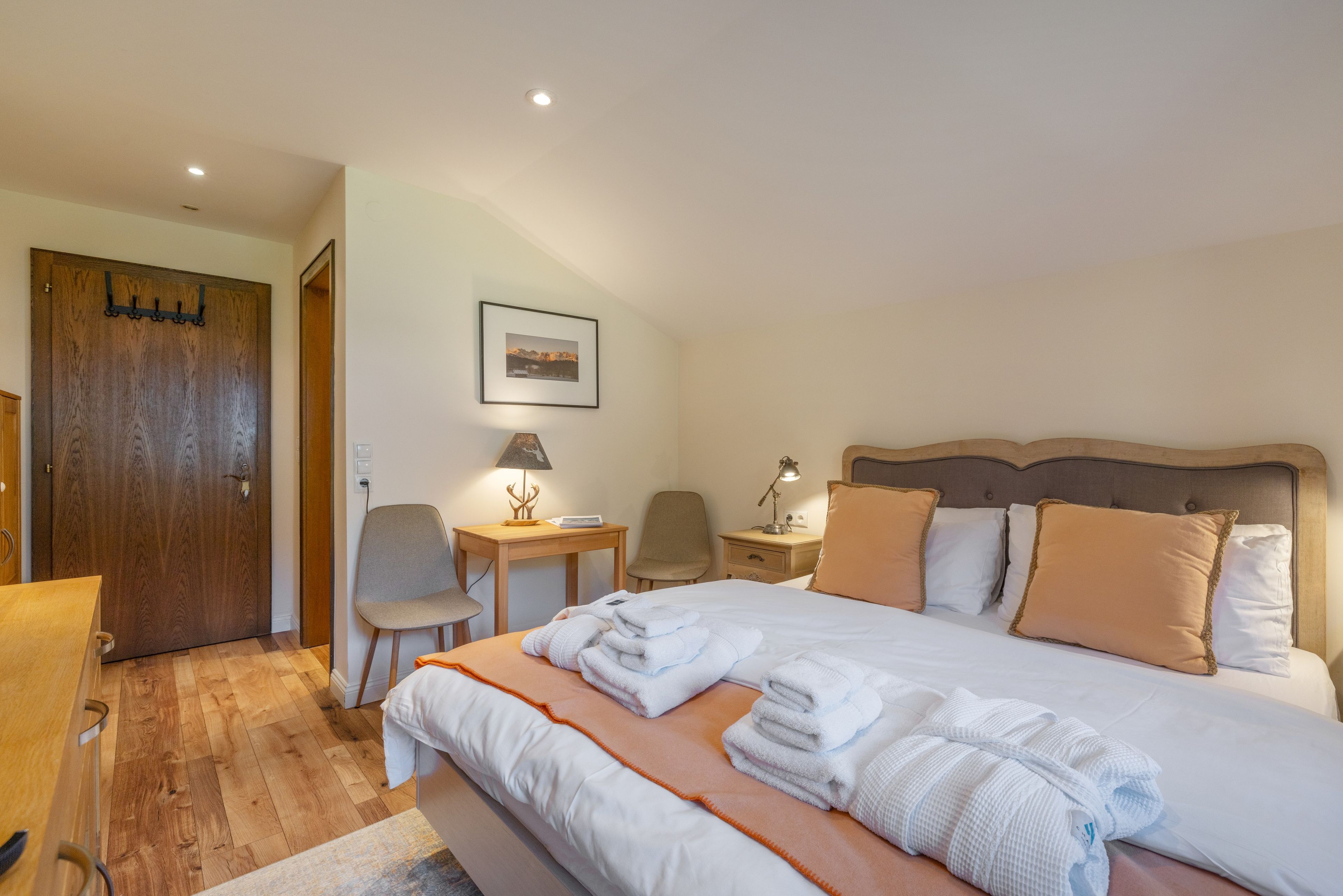 A hotel room with a bed, a desk, a chair, a wooden door, and a framed picture on the wall.