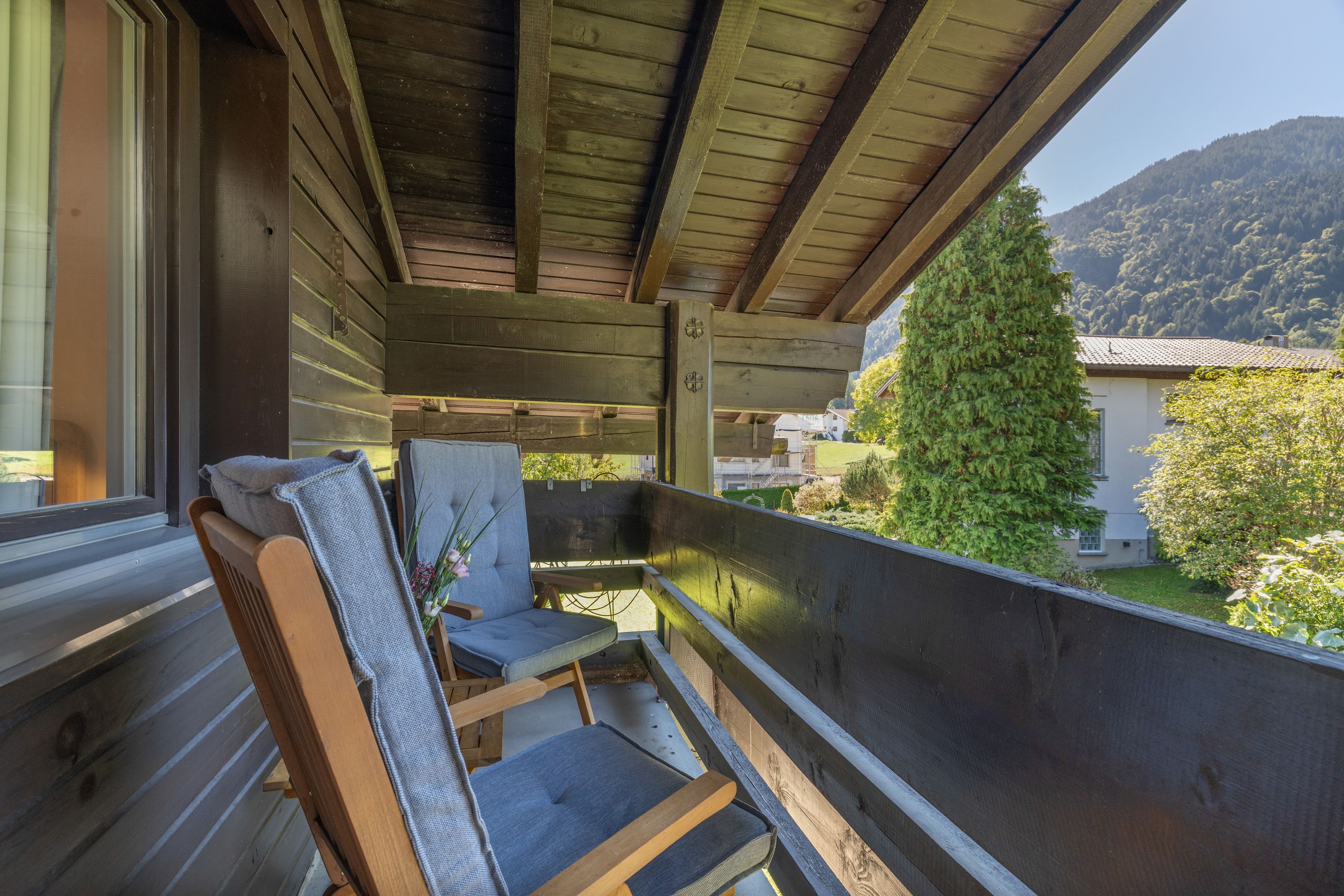 A wooden balcony with a view of a mountain and a house.