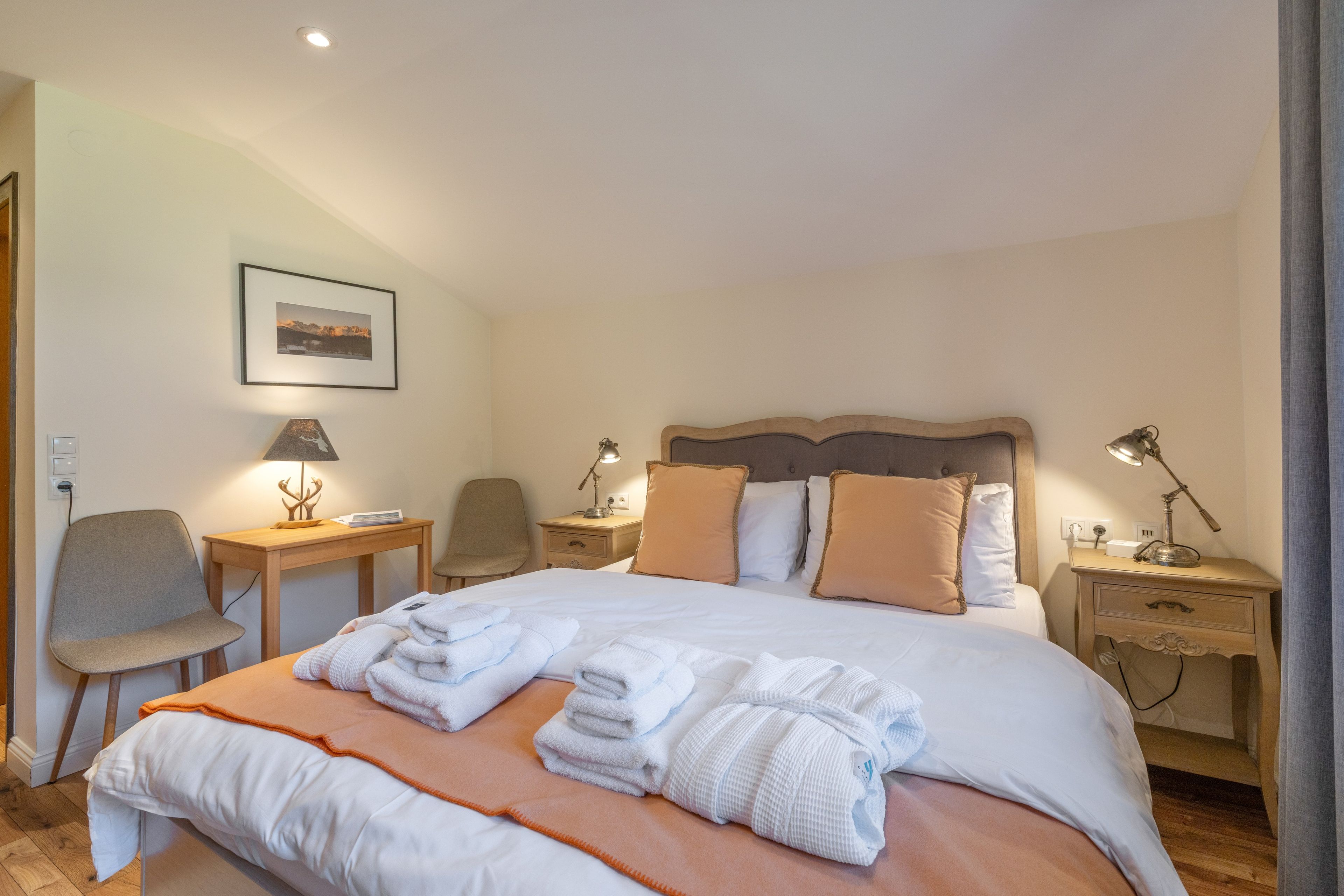 Ein Hotelzimmer mit einem Bett, zwei Nachttischen, einem Sessel, einem Schreibtisch, einer Lampe und einem Bild an der Wand.