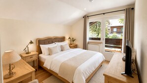 A bedroom with a bed, bedside tables, a desk, a chair, a television, and a window with curtains.