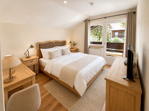 A bedroom with a bed, bedside tables, a desk, a chair, a television, and a window with curtains. - Double Room with Breakfast, Balcony and Mountain View (Vandans)