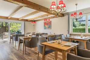 A restaurant with wooden beams, red chandeliers, and a view of greenery outside. - Double Room with Breakfast, Balcony and Mountain View (Vandans)