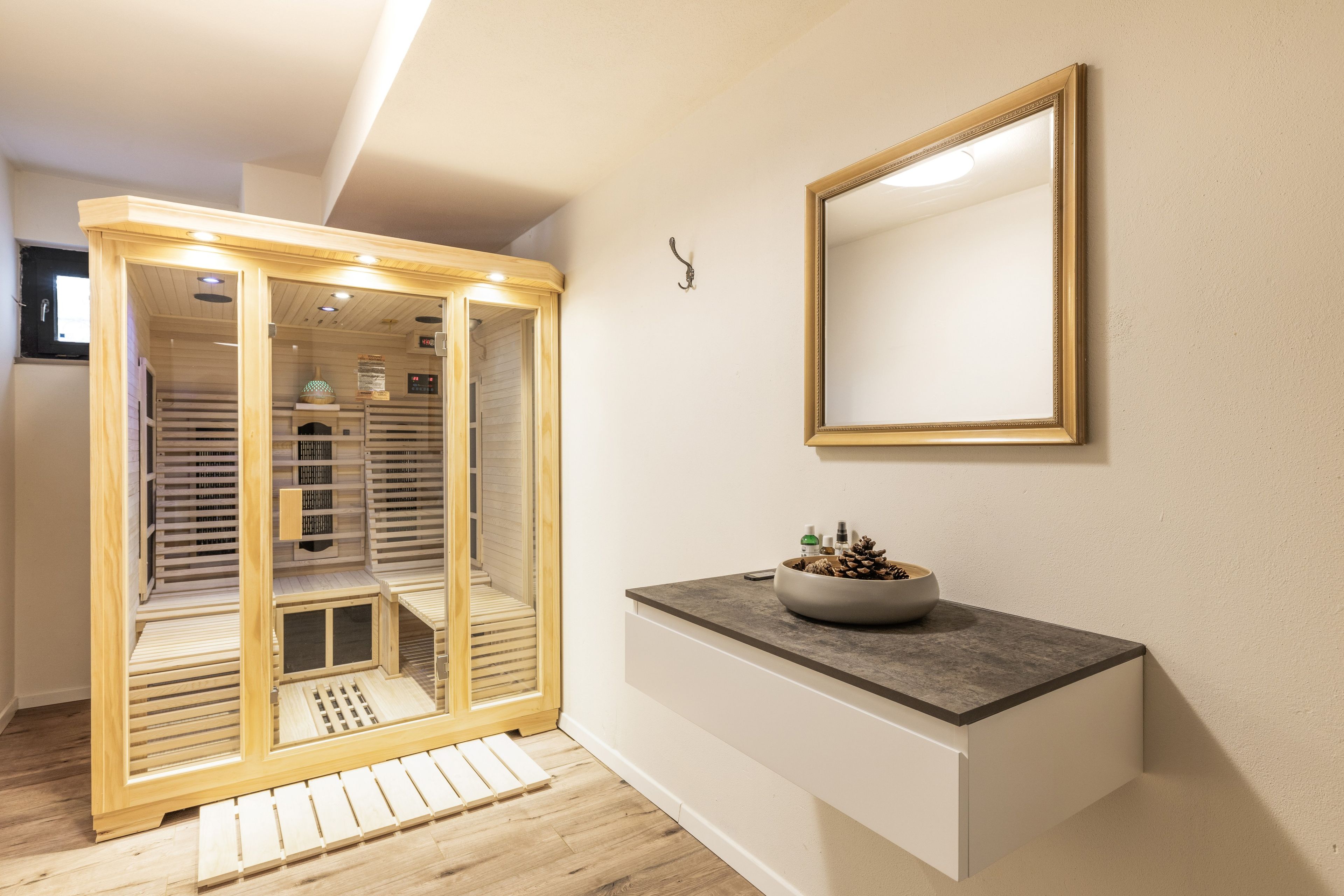 A modern bathroom with a wooden walk-in shower, a mirror, and a countertop with a bowl of pinecones.