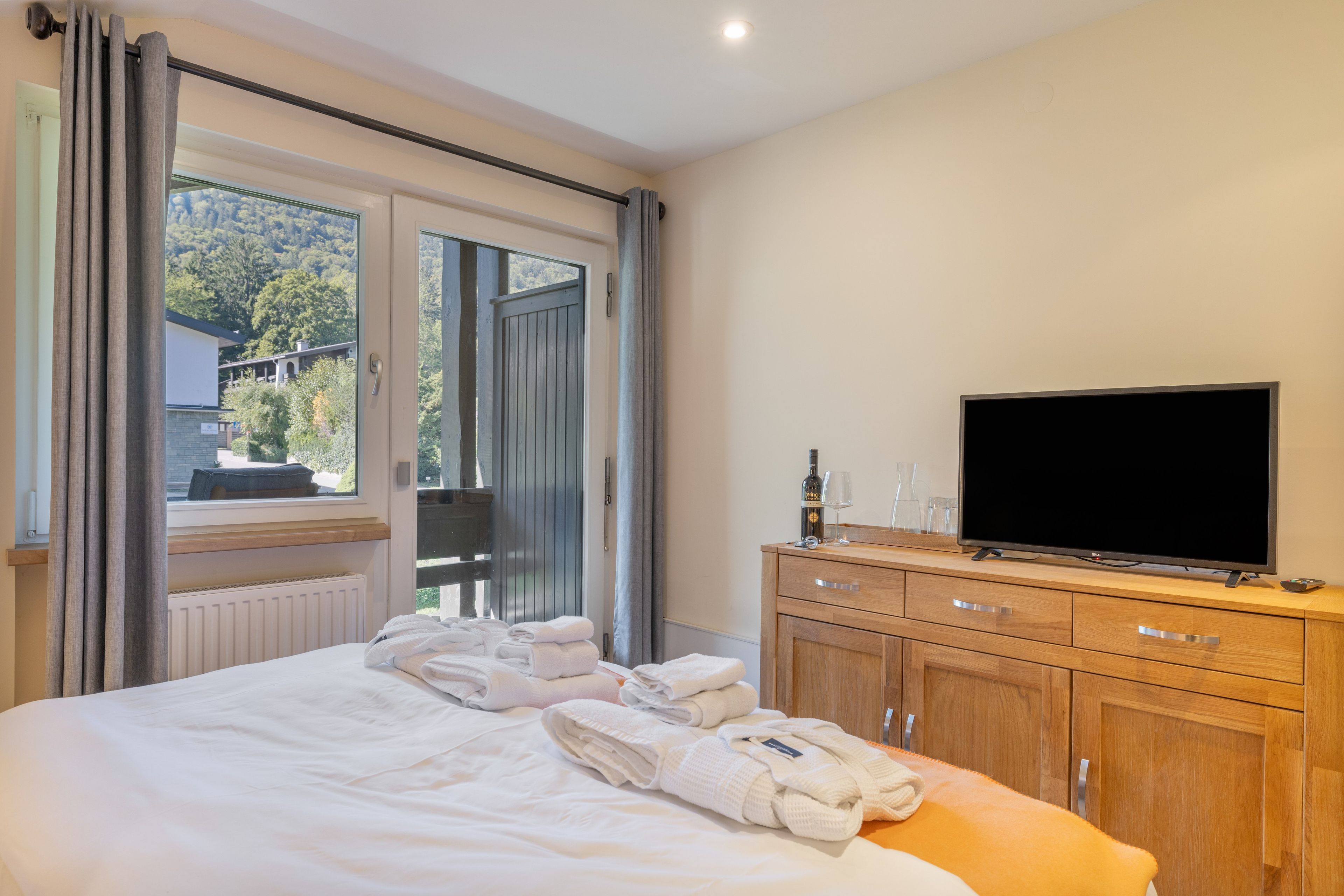 A hotel room with a bed, a TV, a wooden dresser, and a window with curtains.