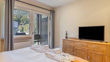 A hotel room with a bed, a TV, a wooden dresser, and a window with curtains.