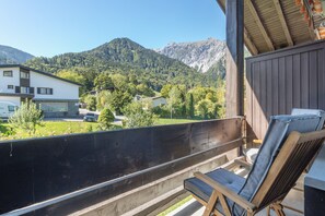 En balkong med en trästol, med utsikt över ett bergigt landskap med hus och en bil.
