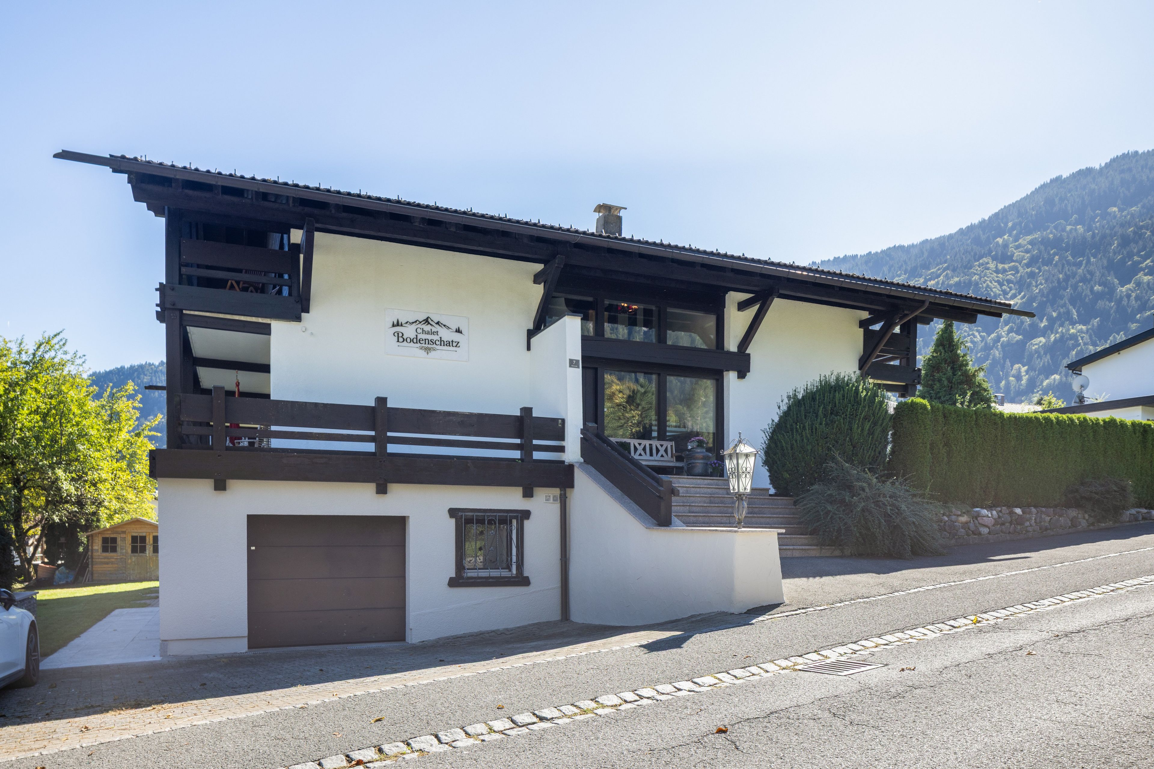 Ein Chalet mit einem Schild, das 'Chalet Bodenschatz' zeigt, einem hölzernen Balkon und einem Berg im Hintergrund.