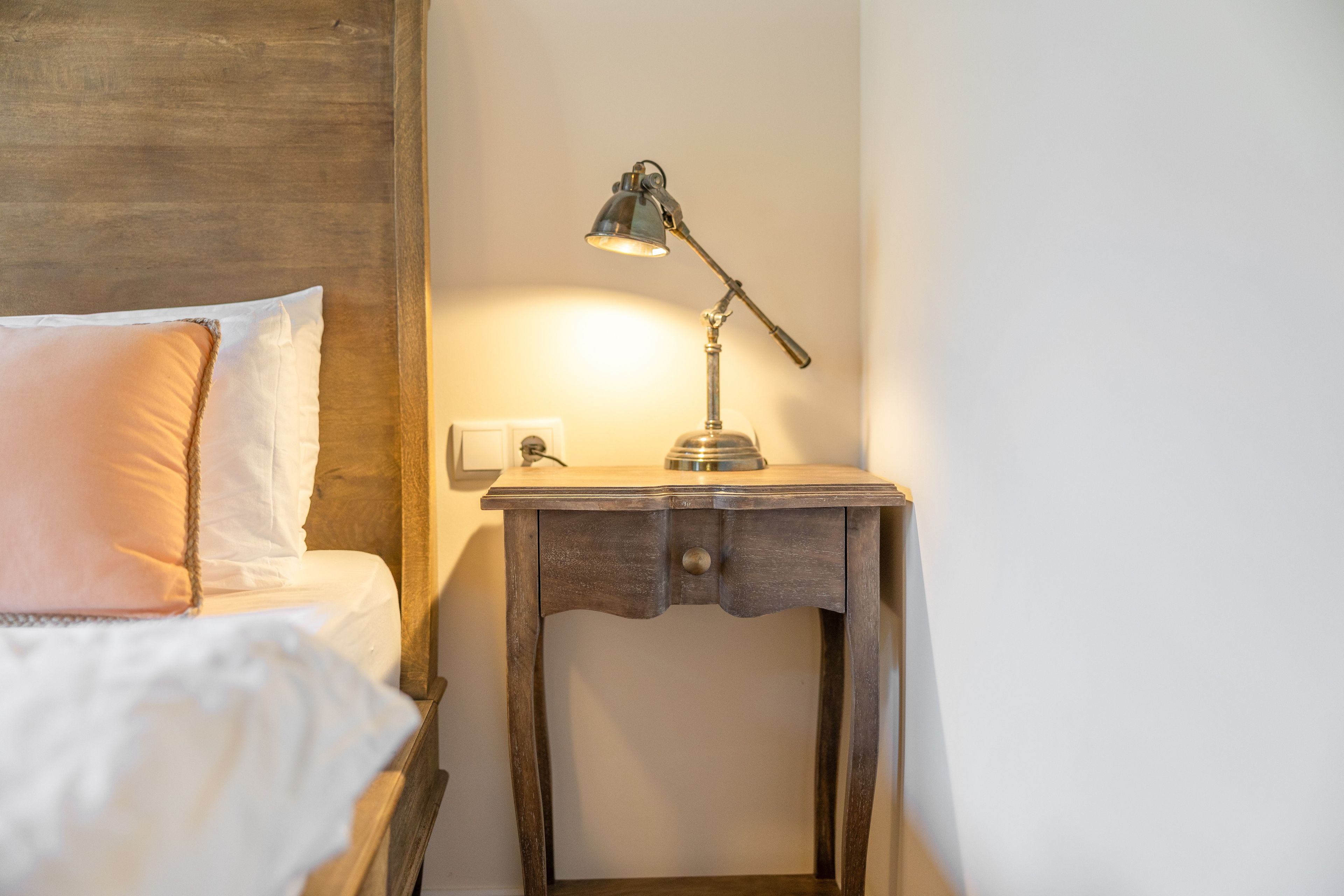 A neatly made bed with a pillow and a small bedside table with a lamp.
