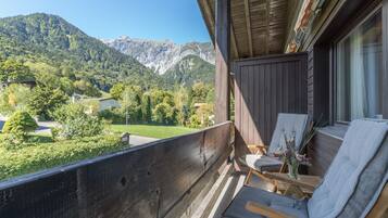 Ein Balkon mit Blick auf eine gebirgige Landschaft, Holzmöbel und ein kleiner Tisch mit einem Blumenstrauß.