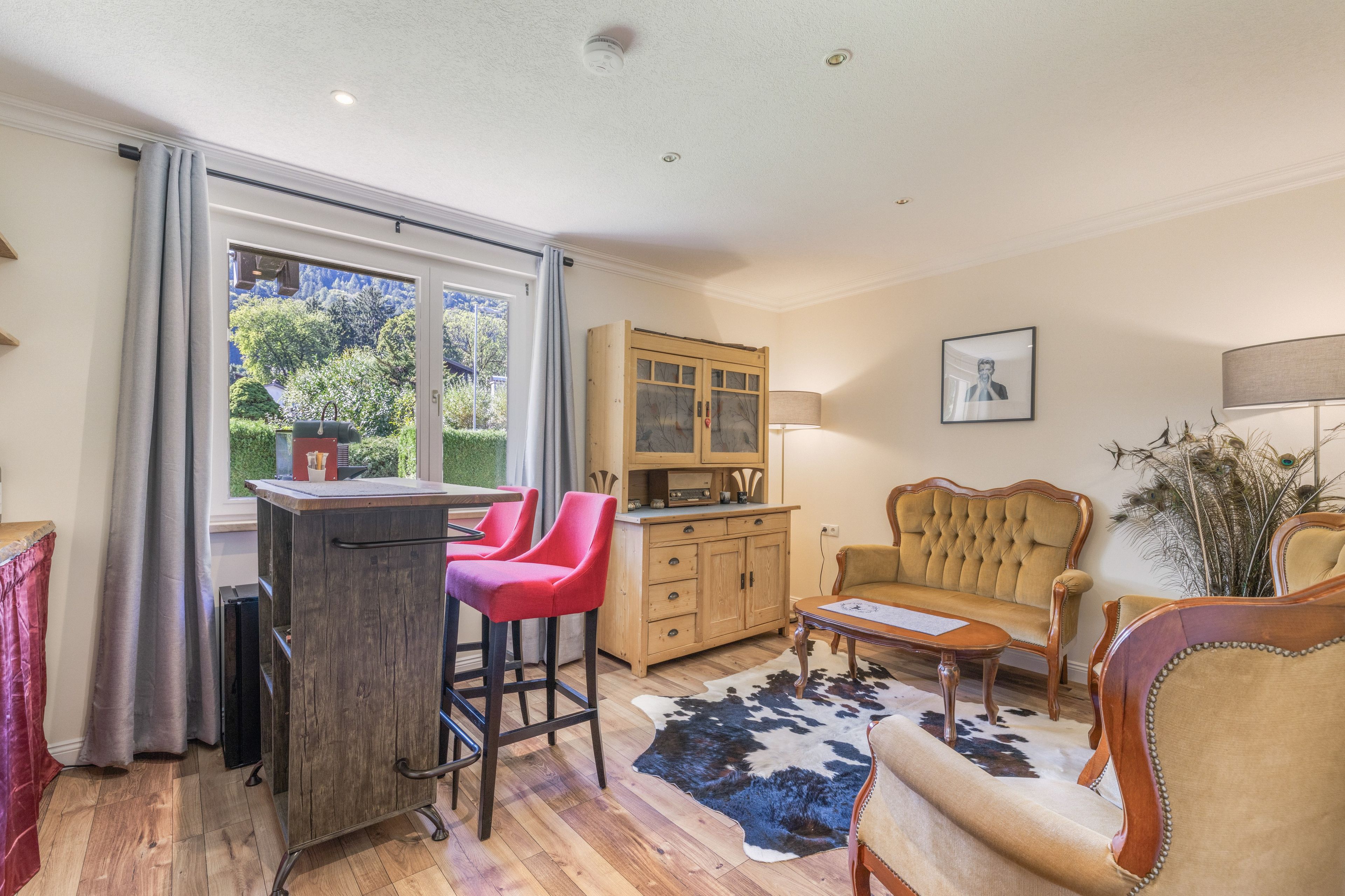A cozy living room with a wooden dining table, red bar stools, a cream sofa, and a peacock feather decoration.