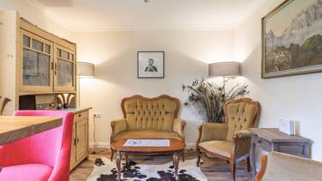 Een kamer met een houten kast, twee fauteuils, een tafel en een schilderij aan de muur.