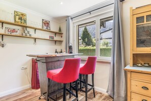 A kitchen with a bar area, wooden shelves with glassware, and a view of a green landscape through a window. - Classic Double Room with Kitchenette, Terrace, and Mountain View (Vandans)