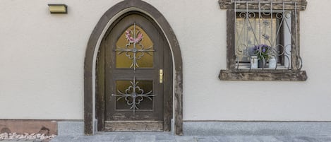 A building with a dark wooden door, a window with metal bars, and a small balcony with potted plants.
